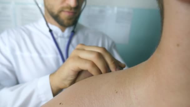 Travailleur médical à l'écoute des battements de coeur de l'homme. Le médecin vérifie le type dans son bureau à l'hôpital. Médecin examinant un jeune patient masculin avec stéthoscope. Gros plan — Video