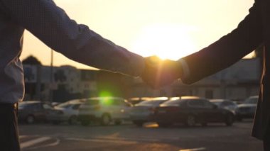 Dışarıda iş tokalaşması ve arka planda güneş ışığı. Erkek kollarını dışarıda sallıyor. Şehir ortamında birbirini selamlayan iki iş adamı. Meslektaşlar şehirde buluşup el sıkışırlar. Kapat.