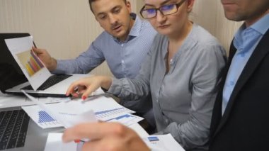 İş arkadaşları, ofiste yapılan takım toplantısında satıştan elde edilen grafikleri analiz ediyorlar. Genç meslektaşlarım masada oturan gelir grafiklerini inceliyor. Profesyonel yöneticiler mali raporları kontrol ediyor. Dolly vurdu.
