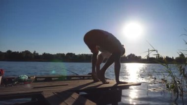 Genç adam gölde tahta bir iskelede bakasana pozu veriyor. Doğada dengede duran bir adam. Arka planda güzel bir manzara. Sağlıklı aktif yaşam tarzı kavramı. Yan Görünümü Kapat