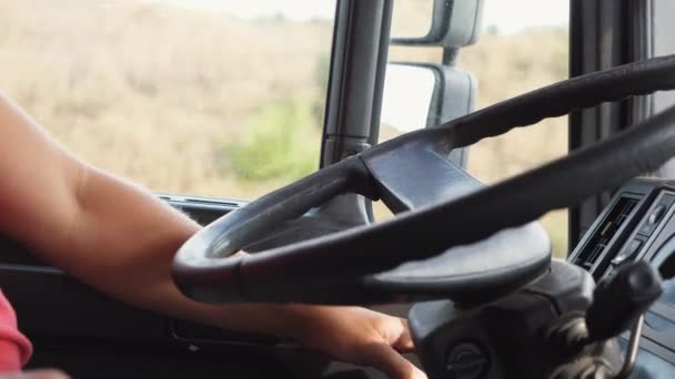 Lorry driver riding to destination at country road. Male hand of trucker holds a big steering wheel while operating a truck through countryside. Concept of logistics and transportation. Close up — Stock Video