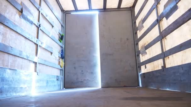 Conductor masculino abriendo la puerta trasera del camión en el campo. Camión estacionado en la carretera del campo. El coche está listo para cargar las mercancías. Vista desde el interior del semirremolque. Concepto de logística y transporte. De cerca. — Vídeo de stock