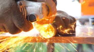 Metal işlemede dairesel testere ile detaylı görüş. Makinistin elleri enstrüman tutuyor ve metali öğütüyor. Garajda ya da atölyede demir kesen bir işçi. Parlak kıvılcımlar uçuşuyor. Kapat.