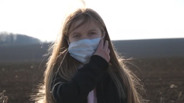 Dışarıda duran tıbbi maskeli küçük bir kızın portresi. Mutlu kadın çocuk, koruyucu maskeyi virüsten çıkar ve gülümse. Koronavirüs ve salgın hastalıklardan korunan sağlık ve güvenlik kavramı — Stok video