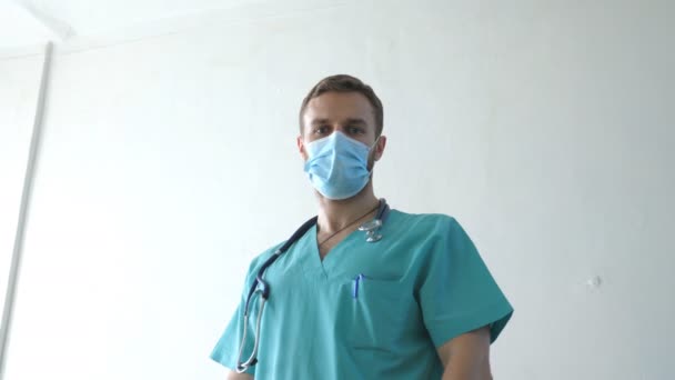 Retrato de un joven médico caucásico con mascarilla médica mira a la cámara. Trabajador médico con máscara protectora del virus. Concepto de la vida de salud y seguridad de la pandemia de coronavirus. COVID-19 — Vídeos de Stock