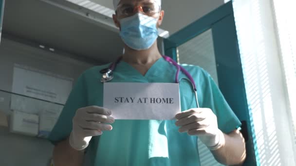 Medic toont poster met een beroep op zelf-isolatie. De mannelijke arts heeft een foto met de inscriptie thuis tijdens de coronavirus epidemie. Concept van de veiligheid van COVID-19 pandemie — Stockvideo