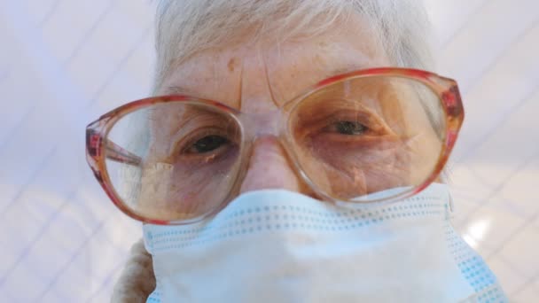 Крупним планом обличчя бабусі в захисній масці від вірусу. Літня жінка дивиться в камеру з пильним зором. Концепція охорони здоров'я та безпеки життя від пандемії. Карантинний коронавірус для літніх людей — стокове відео