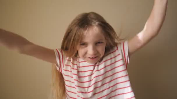 Ευτυχισμένο όμορφο ξανθό κορίτσι κοιτάζοντας στην κάμερα και σηκώνει τα χέρια χαρά επίτευγμα σε εσωτερικούς χώρους. Πορτρέτο του μικρού αστεία θηλυκό παιδί με θετικά συναισθήματα στο πρόσωπό της στο εσωτερικό. Κλείσιμο Αργή κίνηση — Αρχείο Βίντεο