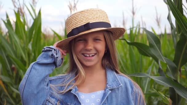 Portrait of attractive happy girl looking into camera and straightening her straw hat against the background of corn field. Little joyful kid with long blonde hair standing in the meadow and laughing — Stock Video
