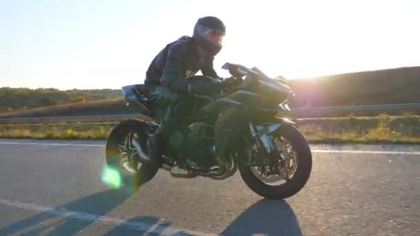 太陽が背景にフレアと高速道路で現代のスポーツバイクに乗って男。オートバイ愛好家は田舎道でバイクレースをしている。旅行中にバイクを運転する男。自由の概念。スローモーション — ストック動画