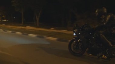 Akşam caddesinde modern siyah spor motosikletli bir adam hızlı gidiyor. Motosikletli, boş yolda motosikletiyle yarışıyor. Farları açık bisiklet süren adam. Özgürlük kavramı. Yan görünüm