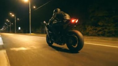 Night City caddesinde, modern motorsikletle hızlı giden bir adam. Motosikletli, boş yolda motosikletiyle yarışıyor. Alacakaranlıkta bisiklet süren adam. Özgürlük ve macera kavramı. Düşük açı. Yakın plan.
