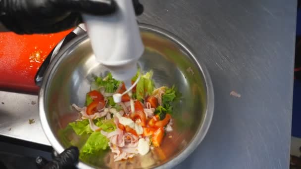 Brazos masculinos de cocinero en guantes vertiendo mayonesa sobre ingredientes frescos en un recipiente de hierro en la cocina. Chef preparando sabrosa ensalada de césar en la cocina. Concepto de cocina de alimentos. Vista superior cámara lenta — Vídeo de stock