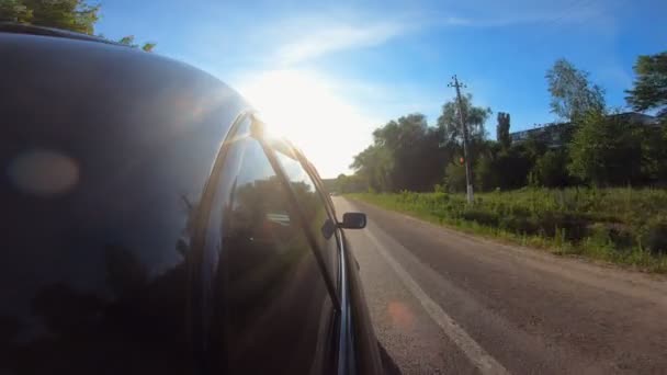 Вид збоку автомобіля на шосе в літній день. Чорний автомобіль швидко їде по сільській проїжджій частині. Автомобіль рухається по автомагістралі через мальовничий ландшафт. Концепція дорожньої подорожі — стокове відео