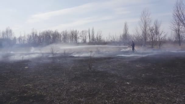 Üniformalı itfaiyeciler, kırsal kesimdeki yangın hortumuyla kuru otları söndürüyorlar. İtfaiyeci ekipmanlarıyla Meadow 'u ateşe veriyor. Çevre sorunları ve küresel ısınma kavramı — Stok video