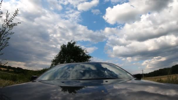 Μαύρο αυτοκίνητο οδήγηση μέσα από την ύπαιθρο με αντανακλάσεις στο καπό και το παράθυρο του συννεφιασμένου ουρανού, σύννεφα και δέντρα. Auto ιππασία κατά μήκος της εθνικής οδού μέσα από γραφικό τοπίο. Θέα από το καπό στο παρμπρίζ — Αρχείο Βίντεο