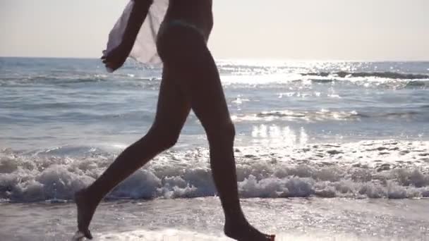 Ноги женщины в бикини и рубашке, бегущей по морским волнам на рассвете. Молодая красивая девушка бегает трусцой и веселится на берегу моря. Летние каникулы или каникулы. Закрыть боковой обзор Медленное движение — стоковое видео
