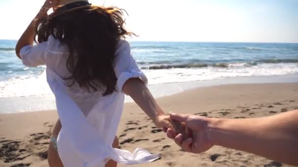 Siga-me tiro de jovem mulher de chapéu puxar o namorado na costa do mar. Menina segurando a mão masculina e correndo na praia para o oceano. Conceito de férias de verão ou férias. Ponto de vista POV Movimento lento — Vídeo de Stock