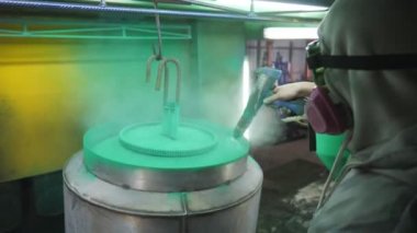 Güvenlik işçileri metal parçaları boyar. Boyacı, boya tabancasından boya püskürterek boyayı boyama odasında detaylandırıyor. Endüstriyel imalatta çalışan teknisyen. Elle püskürtme. Yavaş çekim. Yakın çekim.
