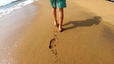 Child walks barefoot on sandy beach, leaving footprints in the wet sand, as gentle waves wash ashore, evoking a sense of freedom and joy in nature