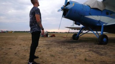 Pilot klasik mavi uçağın yanında duruyor, özelliklerini inceliyor, sonra pervaneye doğru hareket ediyor, havacılıktaki insan ve makine arasındaki bağlantıyı gösteriyor