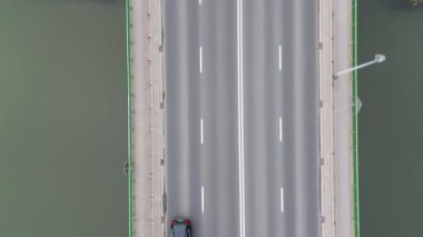 Köprüden geçen bir arabanın hava görüntüsü, trafiğin pürüzsüz akışını gösteriyor, kameralar araçlara yakınlaşıyor, dinamik hareketi ve manzaralı çevreyi vurguluyor.