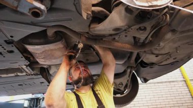 Kahverengi tulumlarda yetenekli tamirciler, tamirat yapmak için araçları özenle kullanır, garaj ortamında karmaşık otomotiv bakım ve uzmanlık sürecini gözler önüne serer..