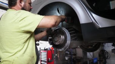 Erkek otomotiv tekerindeki fren bileşenlerini sökmekle meşgul. Bu da alet ve makinelerle dolu yoğun bir garajda uzmanlık gösteriyor.