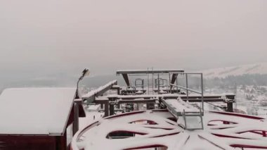 Bir teleferiğin kayak merkezi sahnesi, karlı yamaçlarda kayakçıları ve köyün panoramik manzarasını gözler önüne seriyor, sakin kış atmosferini ve yavaş yavaş alçalmayı vurguluyor.