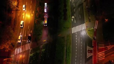 Gece yoğun kavşağın hava görüntüsü, aydınlatılmış araçlarla dinamik trafik akışının gösterilmesi, yol işaretlerini ve kentsel manzara gelişimini vurgulayan kamera tavaları