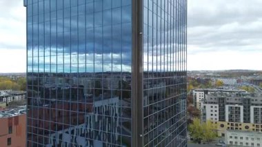 Modern cam gökdelenin hava görüntüsü yansıtıcı cephe sergiliyor, kamera yavaş yavaş mimari detayları vurgulamak ve kentsel manzarayı çevrelemek için yakınlaşıyor, çağdaş tasarım unsurlarını vurguluyor