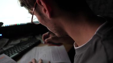 Erkek tüccar birden fazla bilgisayar ekranında hisse senedi grafiklerini analiz ediyor ve kağıda not alıyor. Geceleri emtialar ve döviz çizelgeleri üzerinde çalışan genç bir finans analisti. Bitcoin BTC konsepti.