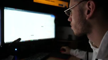 Finans analisti geceleri birden fazla monitörle bilgisayar üzerinde çalışıyor. Gerçek zamanlı emtiaları ve döviz çizelgelerini analiz eden genç bir komisyoncu. Bitcoin BTC ve borsa kavramı. Yavaş çekim.