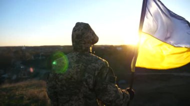 Ukrayna bayrağı sallayan tanınmamış Ukraynalı asker. Askeri üniformalı adam gün batımına karşı bayrak kaldırdı. Rus saldırısına karşı zafer. İstila direnci konsepti. Yavaş çekim.