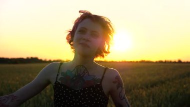 Dövmeli mutlu bayan hippi gün batımında yeşil arpa tarlasından geçiyor. Kısa siyah elbiseli neşeli punk kızı buğday çayırlarında dolaşırken aylaklık ediyor. Yavaş çekim.