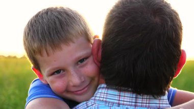 Kırsal kesimde küçük mutlu oğlunun elini tutan genç bir baba. Küçük gülümseyen çocuk kameraya bakıyor ve arka planda parlak güneş ışığına karşı babasına sarılıyor. Aile dinlenmesi kavramı. Kapat..