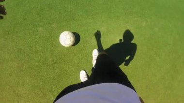 Futbolcu yeşil sahada ustalıkla top sürüyor, dinamik ayak hareketlerini ve kontrollerini gösteriyor, gölgeler hareketi güçlendiriyor ve hareketli sahneleri vurguluyor..