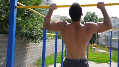 Sporcu dinamik barfiks egzersizi yapıyor, dayanıklılık ve kararlılık sergiliyor, arka planda canlı açık hava eğitim ortamı ve egzersiz ekipmanlarıyla, fitness ilerlemesini ve atletizmi gösteriyor.