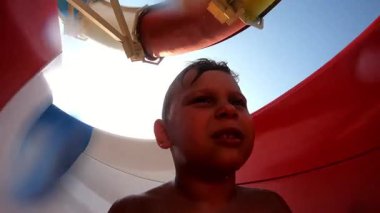 Genç çocuk heyecan verici bir su kaydırağı macerasının tadını çıkarıyor. Renkli dönüşler ve dönüşler yaparken heyecan ve beklenti sergiliyor. Saf neşe ve coşkuyu somutlaştırıyor.