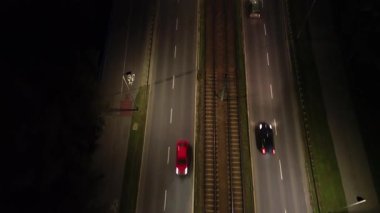 Karanlık bir yol boyunca hareket eden araçların hava görüntüsü, dinamik hareketi kademeli olarak uzaklaşarak gösteriyor, bir gece vakti çevre ve trafik akışını ortaya çıkarıyor.