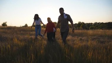 İki çocuklu anne ve baba yaz çayırlarına gidip birlikte vakit geçirmenin tadını çıkarıyorlar. Küçük çocuklu genç ebeveynler gün batımında çim tarlalarında el ele yürürler. Yavaş çekim.