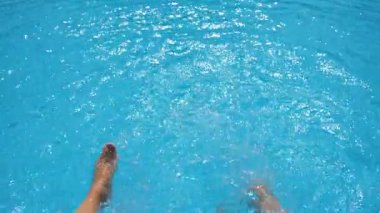 Otelin havuzunda kristal berrak su sıçratan dişi bacaklar. Havzanın kenarında oturan iki arkadaş güneşli bir günde tatilin tadını çıkarıyorlar. Yaz tatili ya da tatil kavramı. Yavaş çekim bakış açısı.