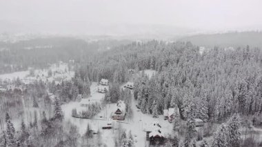 Hava manzarası, karla kaplı ağaçlar ve evlerle kışı yakalar, yavaş yavaş uzaklaşıp, karlı ortamın dingin güzelliğini ve huzurlu ortamını gözler önüne serer.