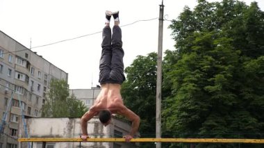 Sporcu dinamik egzersiz yapıyor, paralel çubuklarda şınav pozisyonundan amuda kalkıyor, açık hava eğitim ortamında güç ve denge gösteriyor..