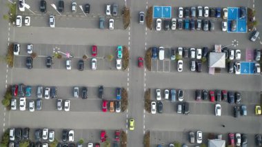 Alışveriş merkezinin yakınındaki işlek otoparkın hava görüntüsü, park yeri dinamiğini ve uzay kullanımını vurgulayan çeşitli park edilmiş araçlar, kamera tavaları