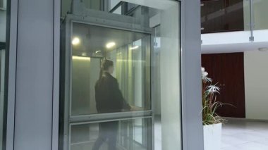 Genç bir kız modern bir asansöre biniyor, kamera tavaları ve zumlar gibi yolculuğunu sergiliyor, sahne boyunca gösterişli tasarım ve ortam aydınlatmasını yakalıyor.