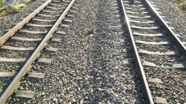 Demiryolu rayları, demiryolu altyapısının karmaşık detaylarını yakalamak için aşamalı olarak yaklaşan, dokulu çakıl ve metal rayları gösteren dinamik bir sahnede kesişir.