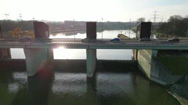 Köprünün üzerinden geçen araçların hava görüntüsü, aşağıdaki akan suyu gösteriyor ve kamera sahnenin derinliğini ve detaylarını düzgün bir şekilde yansıtıyor.