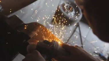 Profesyonel tamirci ya da tamirci atölyede testereyle metal kesiyor. Erkek kaynakçı çeliği elektrikli çarkla kesiyor ve garajda koruyucu gözlük takıyor. Turna atışı Ağır çekim.