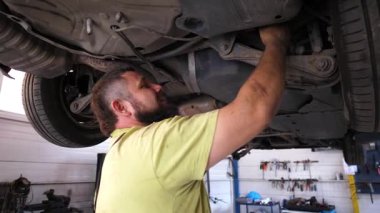 Tamirci, otomotiv hizmetinde kullanılan teknik uzmanlığı ve araçları vurgulayarak, hassasiyet ve özenin önemini vurgulayarak, bir aracın altından tamir etmekle meşgul.